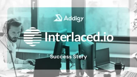 Bearded man wearing headphones works focused at a multi-monitor desktop workstation in a bright office, using a mouse. Interlaced and Addigy logo overlay